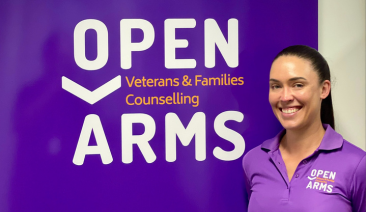 A woman stands by an Open Arms sign