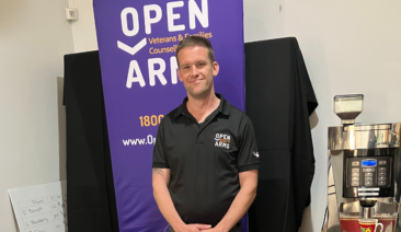 A man stands in front of an Open Arms banner